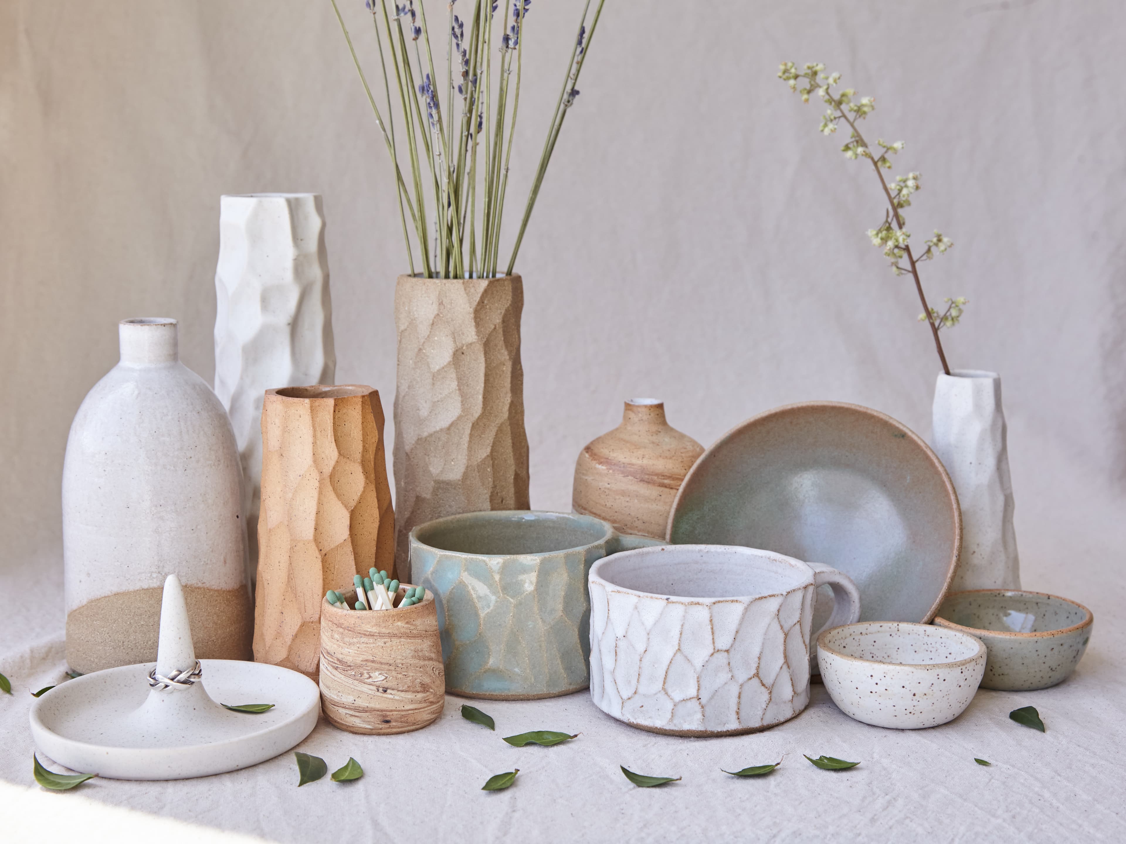 A collection of handmade ceramic vases, bowls, and cups styled together on linen