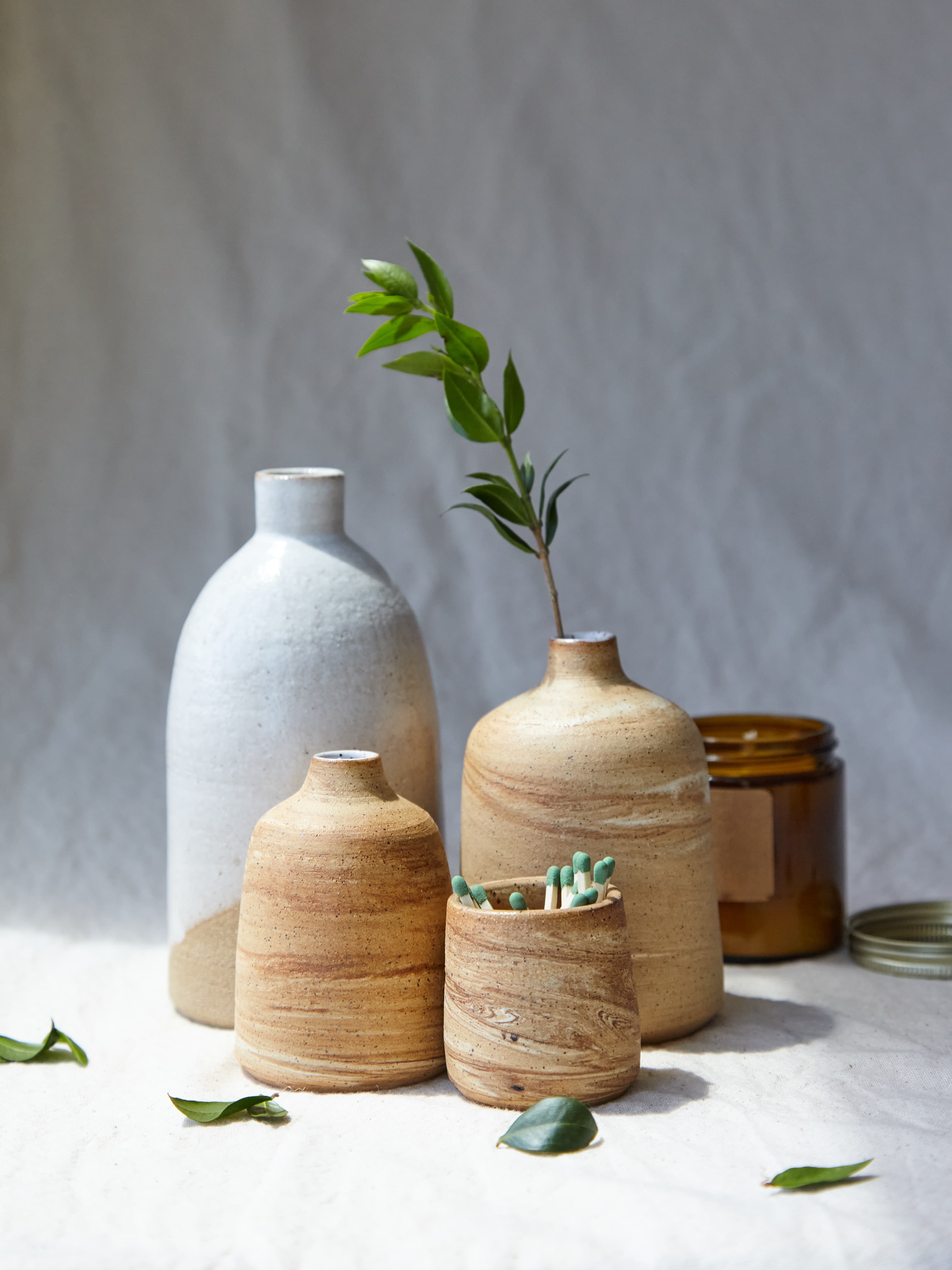 A cluster of handmade ceramic bud vases with a sprig of greenery and a jar of matches